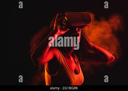 Anonymous astonished ethnic female with open mouth exploring virtual reality in headset on black background Stock Photo