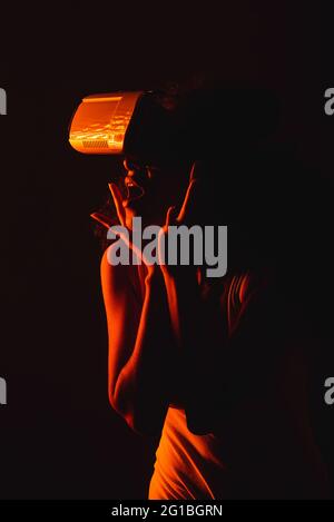 Anonymous astonished ethnic female with open mouth exploring virtual reality in headset on black background Stock Photo