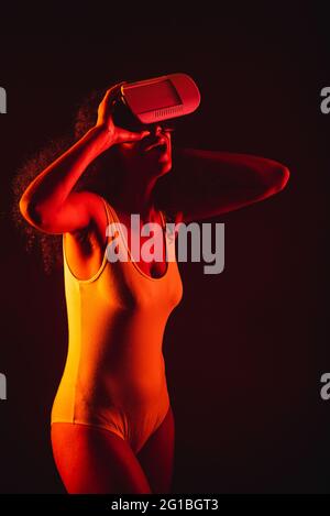 Anonymous astonished ethnic female with open mouth exploring virtual reality in headset on black background Stock Photo