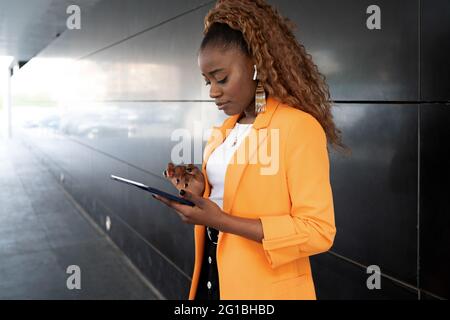 African American female in elegant stylish wear surfing tablet while standing in corridor Stock Photo