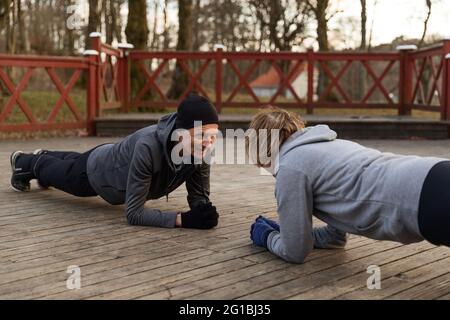 Senior couple doing elbow plank exercise on wooden floor during active training in park in autumn day Stock Photo
