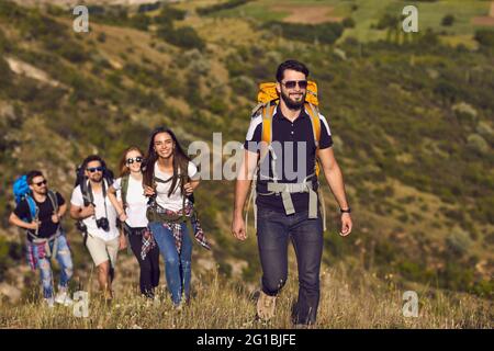 Group of smiling young travelers hikers tourists with backpacks hiking with in row