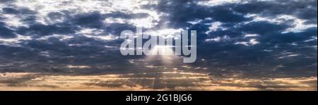 Panorama of orange and dark blue dramatic sky with clouds at sunset, summer evening. The sun's rays break through the dark clouds. Blur in motion. Stock Photo