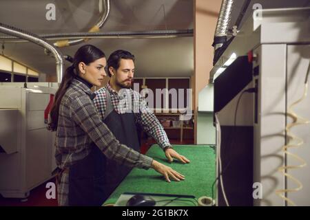 Two shoe factory workers checking work of cutting machine at manufacturing workshop Stock Photo