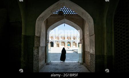 Isfahan, Iran - May 2019: Unidentified iranian woman in hijab black dress walking towards the courtyard of the Great Mosque of Jameh Mosque of Isfahan Stock Photo