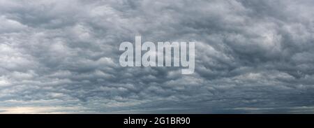 Low gray stratocumulus clouds covered the whole sky. Dark overcast sky panorama. Wide image of scenic rainy clouds. Dramatic sky before the rain. Stock Photo