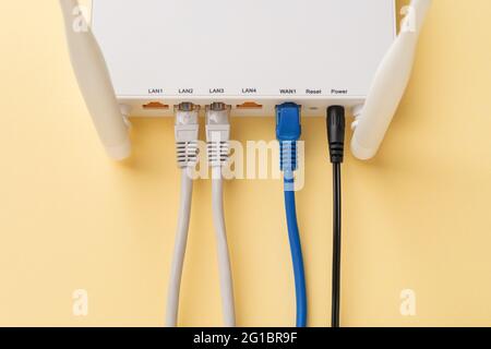 White Wi-Fi wireless router with connected network and power cables on a yellow background. Home and office wlan router with inserted internet cables. Stock Photo