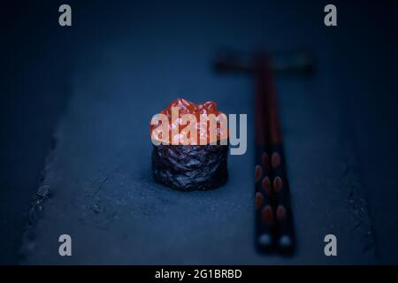 One eggs salmon or ikura roe sushi, on black tray with dark wood chopsticks. Black background, minimalist. Stock Photo