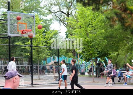 multiple basketballs fly through the air towards the hoop as one goes in to score on a playground basketball court in new york city as youth players l Stock Photo