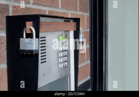 Building enterphone or intercom, closeup. Perspective view of autodialer interphone system with padlocks and rusty security bar, mounted on brick wall Stock Photo