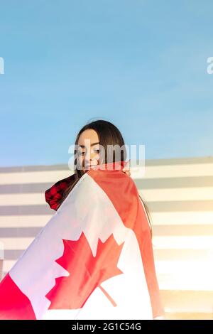 Young millennial brunette woman holding The National Flag of Canada. Canadian Flag or the Maple Leaf. Tourist traveler or patriotism. Immigrant in a free country. Independence day 1th july. Canada day, copy space. National holiday Flag blowing in the wind Stock Photo