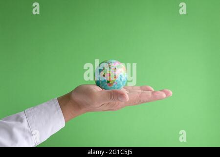 Businessman holding the world in the palm of hand. Green background. Copy space. Stock Photo