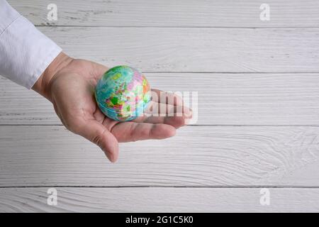 Person holding the world in his hand. White wood background. Copy space. Stock Photo