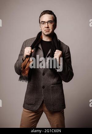 Portrait of dissatisfied, arrogant businessman in jeans, checkered plaid jacket and scarf standing looking at camera Stock Photo
