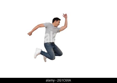 Full length portrait of an excited young Asian man in gray t-shirt jumping while celebrating success or dancing with music isolated over white backgro Stock Photo