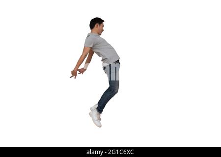 Full length portrait of an excited young Asian man in gray t-shirt jumping while celebrating success or dancing with music isolated over white backgro Stock Photo