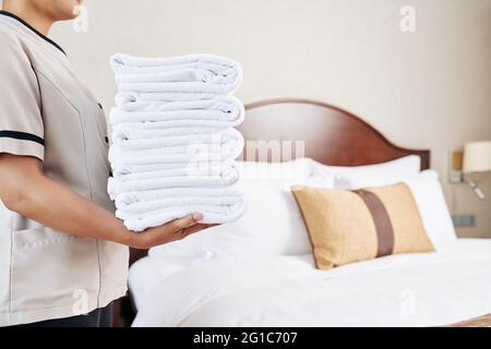 Maid carrying stack of fresh clean fluffy towels to hotel room, selective focus Stock Photo