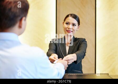 Smiling receptionist giving electronic key card to hotel guest with two hands Stock Photo