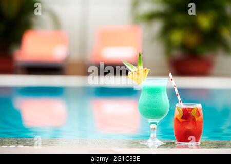Decorated glasses of sweet delicious tourquoise and red fruit cocktails on edge of swimming pool Stock Photo