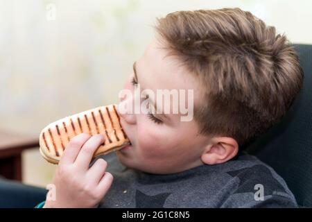 A Hungry boy eating a hot dog at home kid eats a hot-dog sandwich.Indoors shot.Closeup. Stock Photo