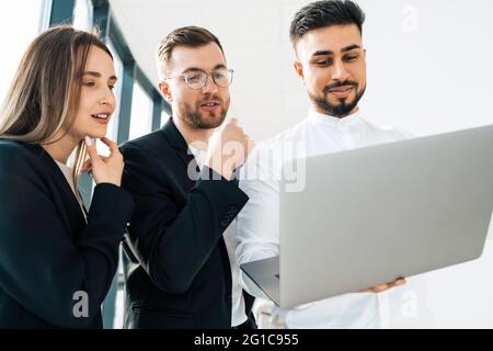 Three employees of the company are looking at laptop and thinking about new project Stock Photo