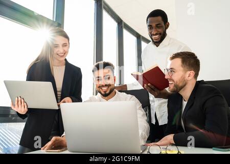 Employee of the software development firm are discussing new projects in the office over notebooks Stock Photo