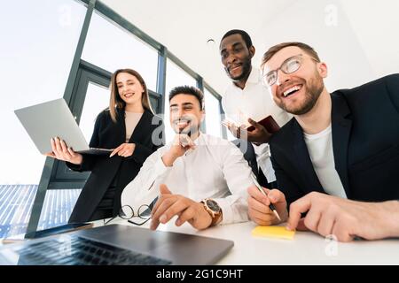 Young multiracial ambitious team of programmers are thinking about a new project while sitting behind laptop Stock Photo
