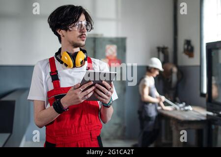 Portrait of young worker standing indoors in factory looking at camera. Stock Photo