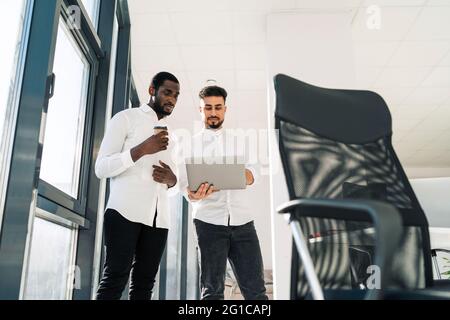 Two serious businessmen are standing in the office with laptop and are discussing about new project Stock Photo