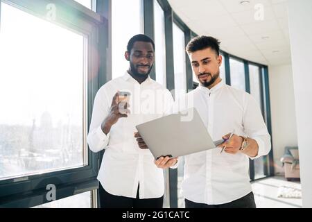 Two businessmen are standing with laptop in the office with panoramic windows Stock Photo