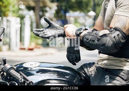 Hands of motorcyclist sitting on bike and putting on riding gear like forearm guard pads and leather gloves Stock Photo