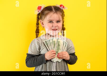 Children and financial responsibility, little girl on a yellow background with dollars in her hands, financial literacy in a child. new Stock Photo