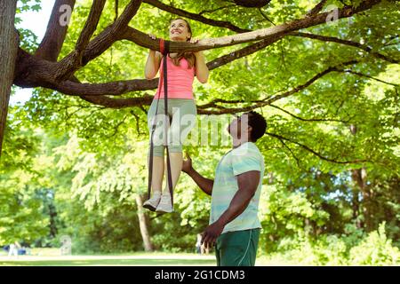 Woman doing pull-up assisted by her fitness coach on tree Stock Photo