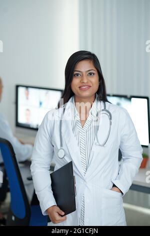Positive young female physician standing in medical office with clipboard in hand ready to visit sick patients Stock Photo