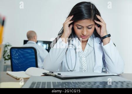 Stressed young general practitioner trying to concentrate on work when reading medical history of patient Stock Photo