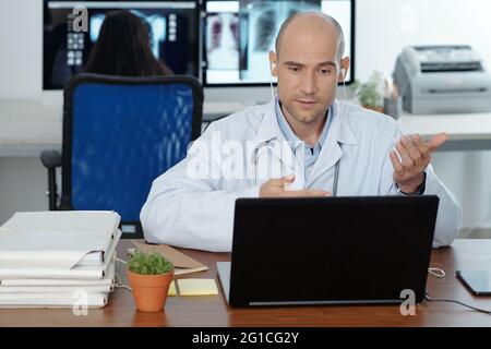 Doctor sitting at desk, having video call with colleague or patient and discussing disease treatment Stock Photo