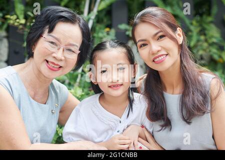 Portrait of cheerful pretty little girl, her mother and grandmother spending time outdoors in backyard or park Stock Photo