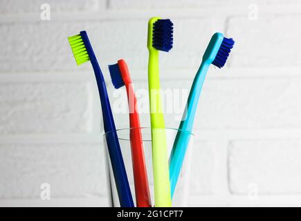 Set of plastic multicolored toothbrushes - green, blue, red, purple - in the transparent glass on a white background. Cup with four bright colorful so Stock Photo