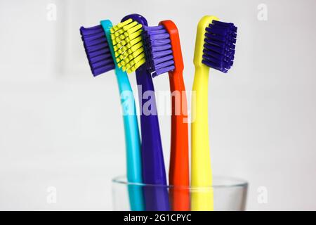 Set of plastic multicolored toothbrushes - green, blue, red, purple - in the transparent glass on a white background. Cup with four bright colorful so Stock Photo