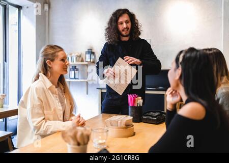 Waiter talking with female customers while taking order in restaurant