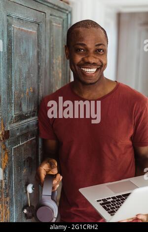 Portrait of smiling businessman holding headphones and laptop at home Stock Photo