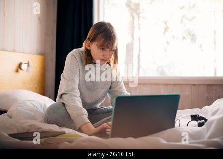 Teenage girl using laptop while doing homework in bedroom Stock Photo