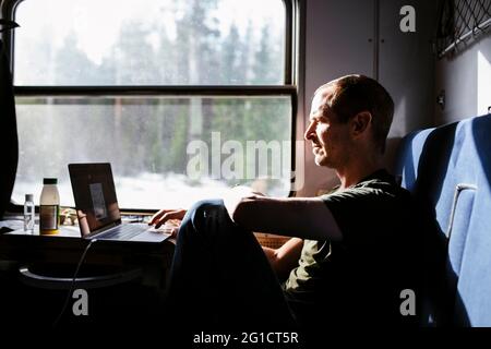 Businessman using laptop while sitting by window in train Stock Photo