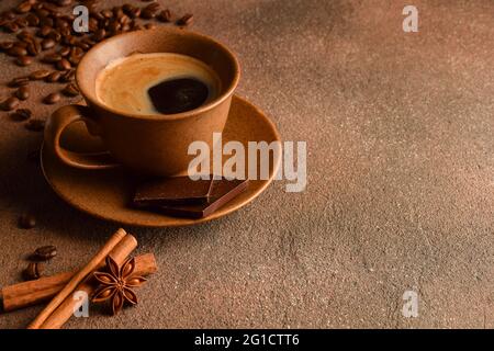 Ceramic coffee cup with saucer, pieces of chocolate, coffee beans, cinnamon and anise on a stone surface. On the right is an empty ad space Stock Photo