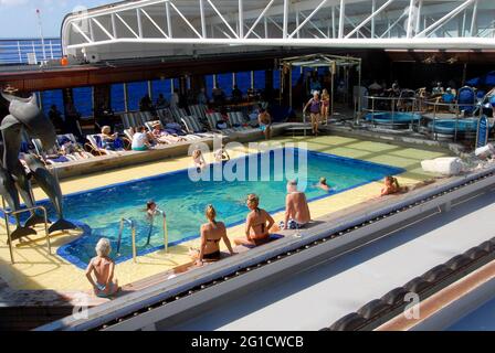 Passengers around the covered pool on a cruise liner with the roof covering retracted to allow the sunshine in, Caribbean Stock Photo