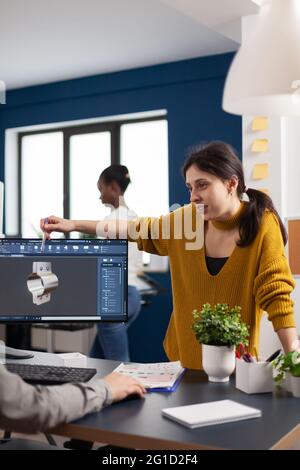 Team discussing about industrial project using dual monitors setup to desing 3D gears and metalic clamp in CAD software. Woman industrial engineer project manager working in creative office Stock Photo