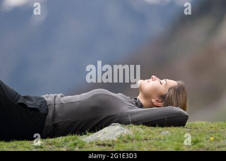 Side view portrait of a relaxed trekker resting lying on the grass in the mountain Stock Photo