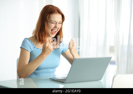 Excited woman using laptop celebrating success in a hotel room Stock Photo