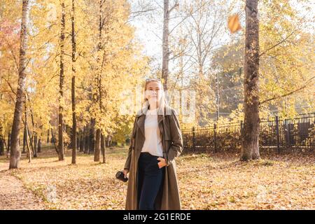 Business woman in coat drink coffee in the park, front view. Autumn park, sunny day. Stock Photo