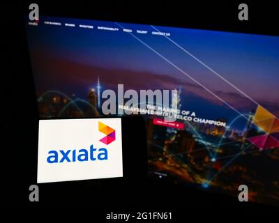 Person holding cellphone with logo of Malaysian carrier Axiata Group Berhad on screen in front of business webpage. Focus on phone display. Stock Photo